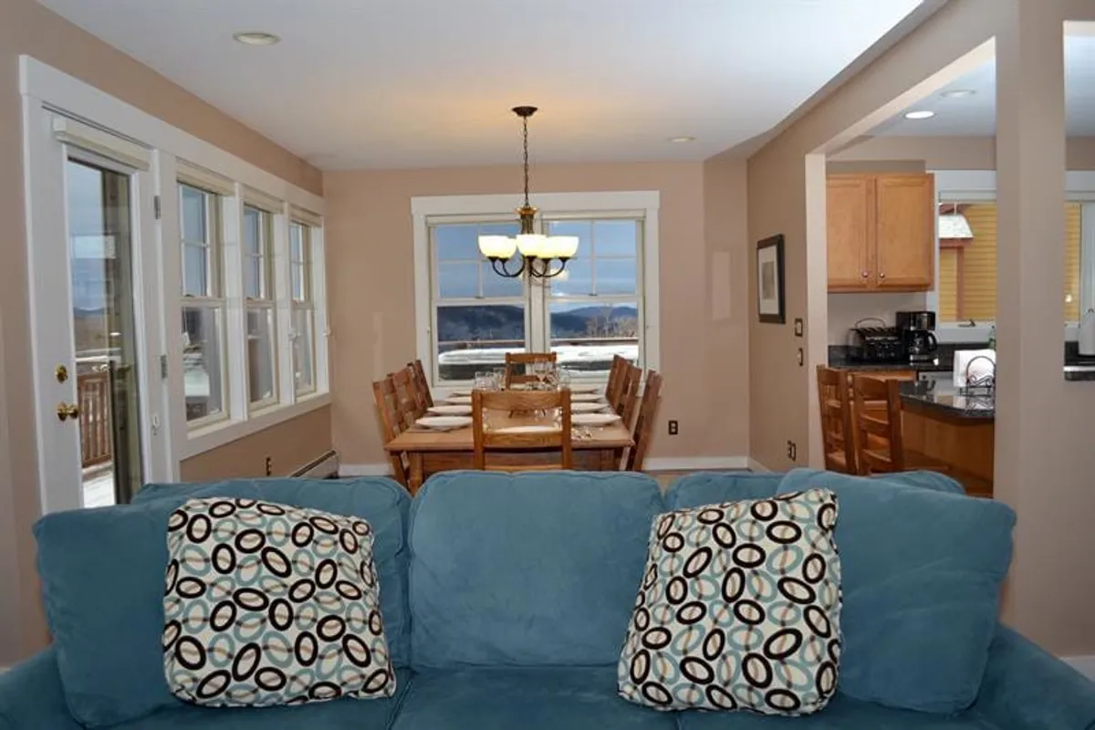This image showcases an inviting dining area with a dining table, a comfortable sofa, and large windows that let in plenty of natural light. The presence of expansive windows creates a visual connection to the outdoors, suggesting easy access to nature and the surrounding landscape.