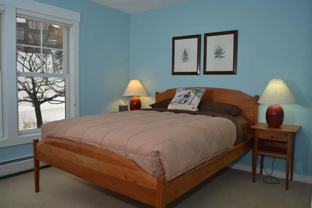 An inviting bedroom with a cozy bed, window views, soft lighting from table lamps, and tasteful artwork adorning the walls. The scene is designed for relaxation, reading, or a good night's sleep, reinforcing the sense of home-away-from-home.