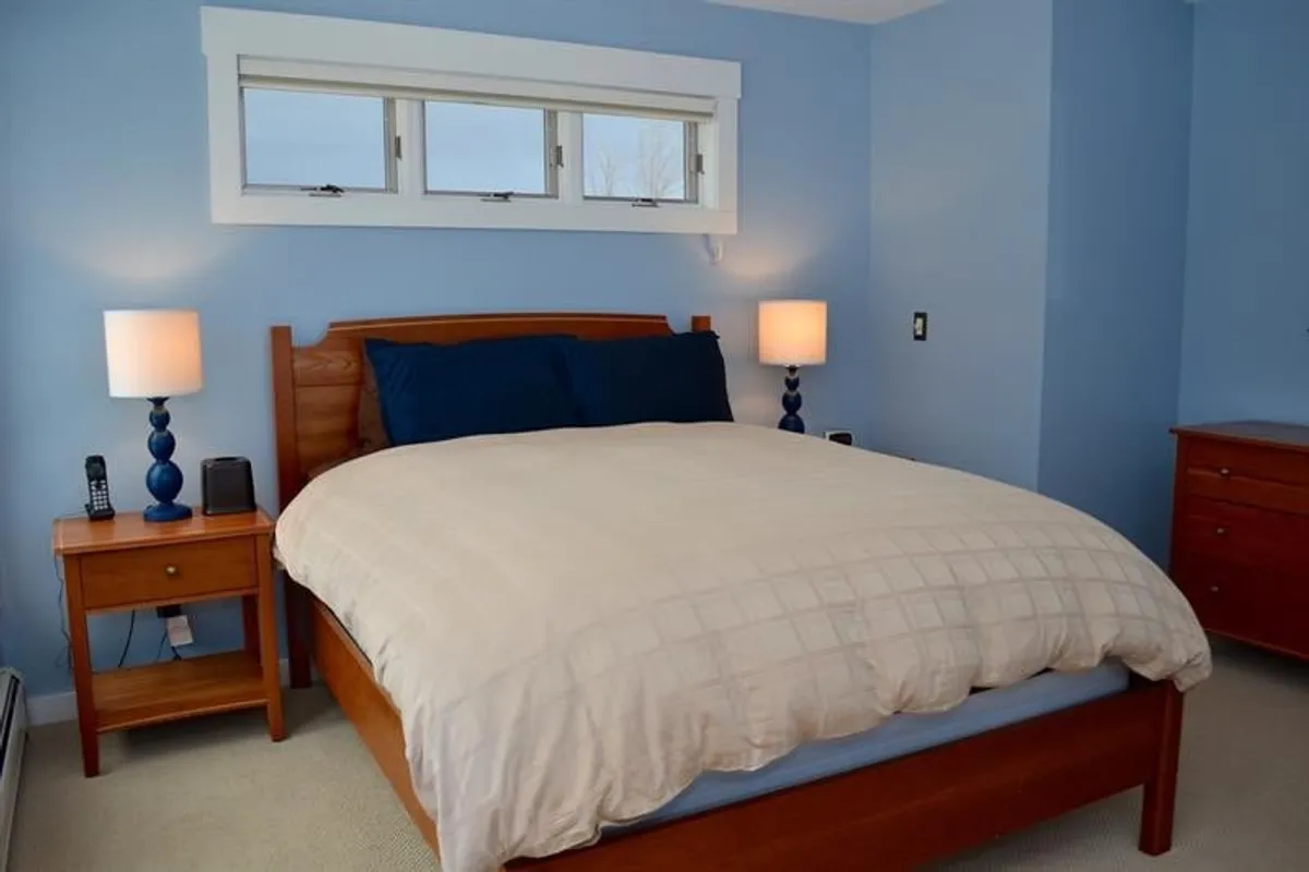 A peaceful bedroom scene featuring a comfortable bed flanked by nightstands and lit by warm lamps, with a large window filling the room with natural light. The layout invites restful moments and relaxed conversation, highlighting privacy and comfort.