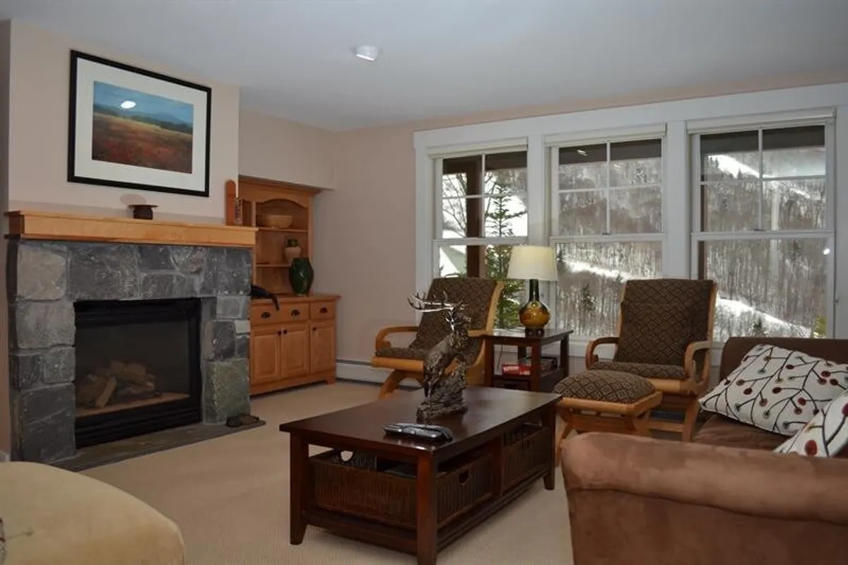 A cozy nook with plush armchairs set around a stone fireplace, a coffee table, and a decorative statue, accompanied by a window offering outdoor views. The arrangement encourages conversation, relaxation, and taking in the natural scenery.