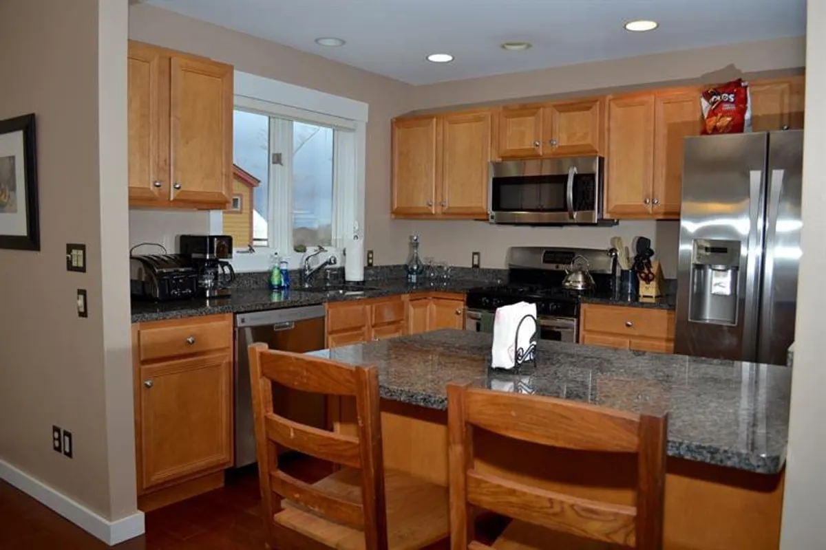 A modern kitchen setup with granite countertops, stainless steel appliances, wooden cabinets, and casual bar stools. The open layout encourages socializing, cooking, and informal gatherings, reflecting the home's versatility for group activities.