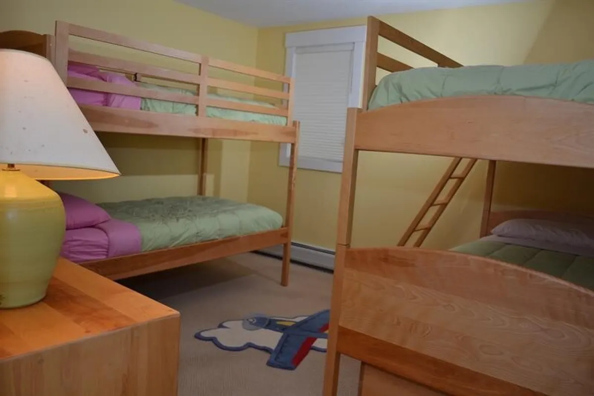 A playful bunk room featuring stacked beds, a lamp, and a soft rug, evoking a sense of fun and coziness. The space invites late-night chats, games, and a sense of camaraderie for children or friends.