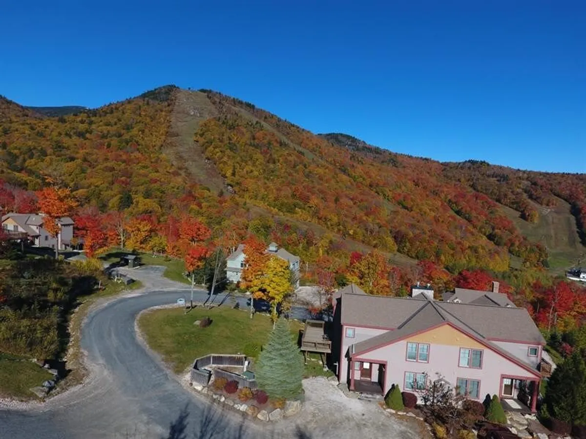 This image captures a stunning mountain landscape with the property's architecture nestled among colorful autumn foliage. A roadway winds through the area, creating a sense of access and connection to the natural surroundings. The view conveys tranquility and adventure, with hints of outdoor activities and communal spaces.