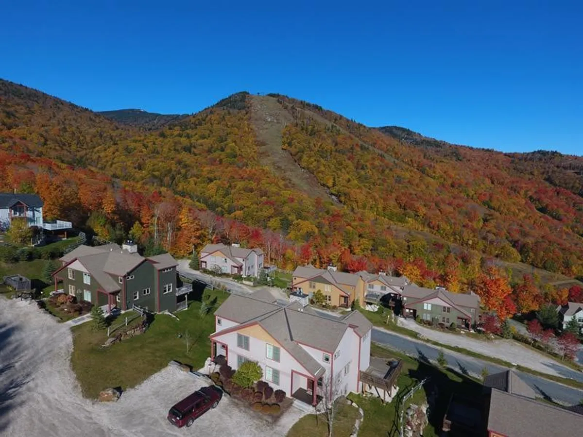 A picturesque exterior view featuring colorful foliage, majestic mountains in the background, and inviting homes nestled in nature. The setting exudes tranquility and showcases the beauty of outdoor living across seasons.