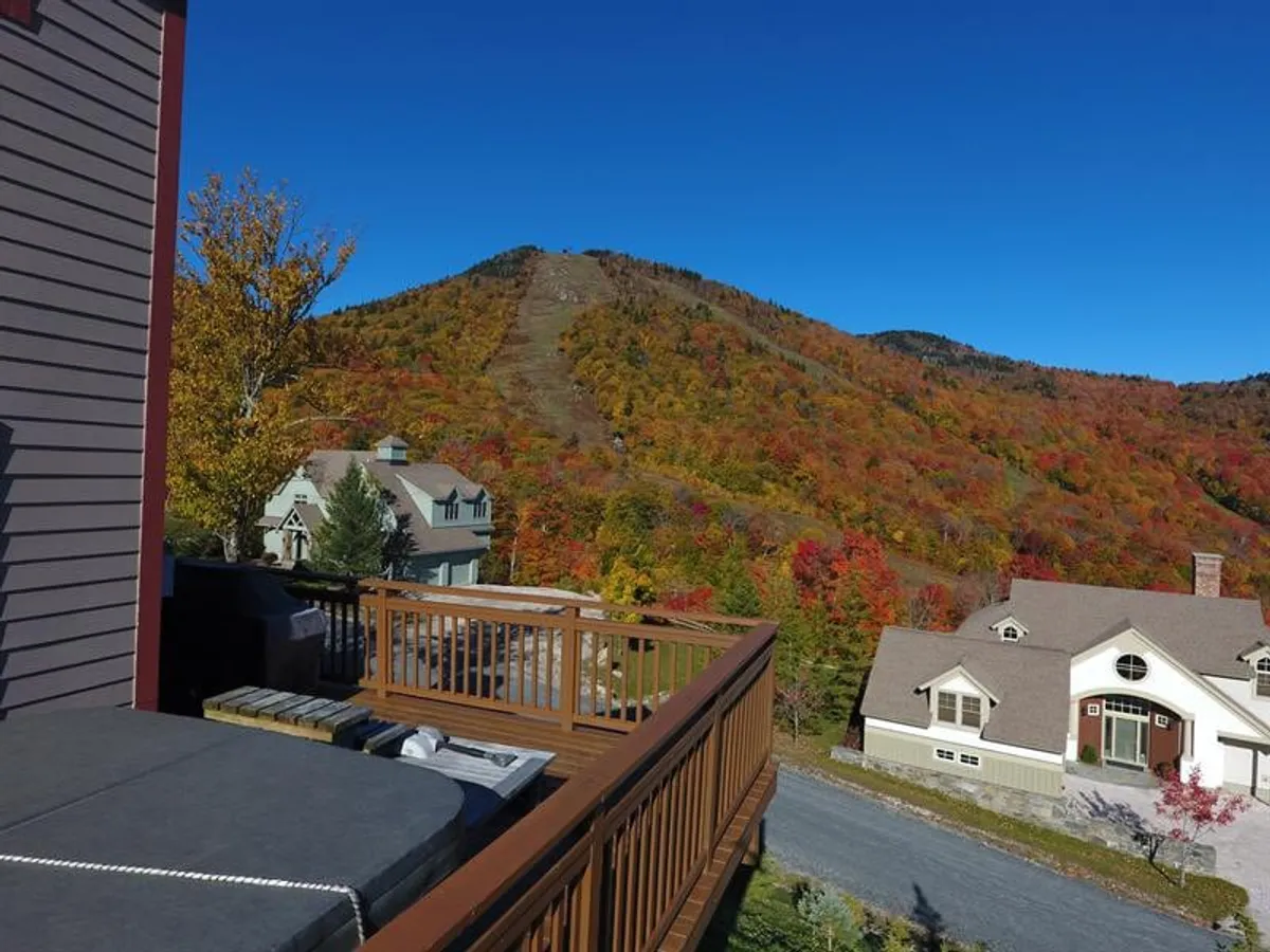 An inviting deck area with seating overlooks stunning mountain vistas and colorful foliage. The scene is set for outdoor relaxation, grilling, or dining while marveling at breathtaking sunsets.