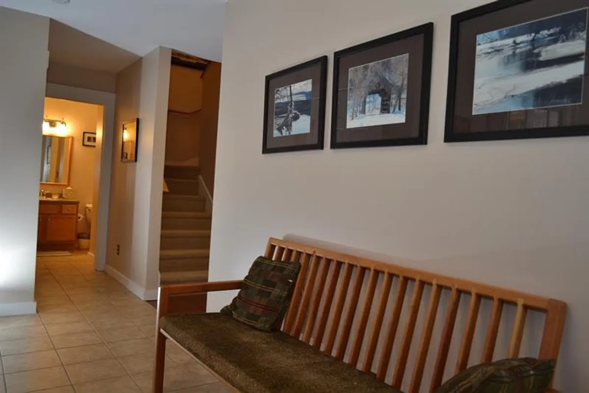 A cozy interior entryway with a wooden bench, framed photographs, and a staircase ascending, evoking a warm welcome and a place to pause before or after outdoor activities.